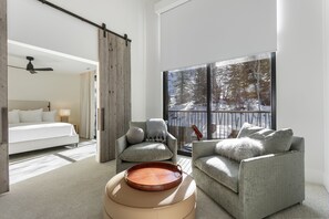 Enjoy a serene view of the snowy landscape from the large window in this cozy retreat, featuring a comfortable seating area and a stylish bed with white linens.