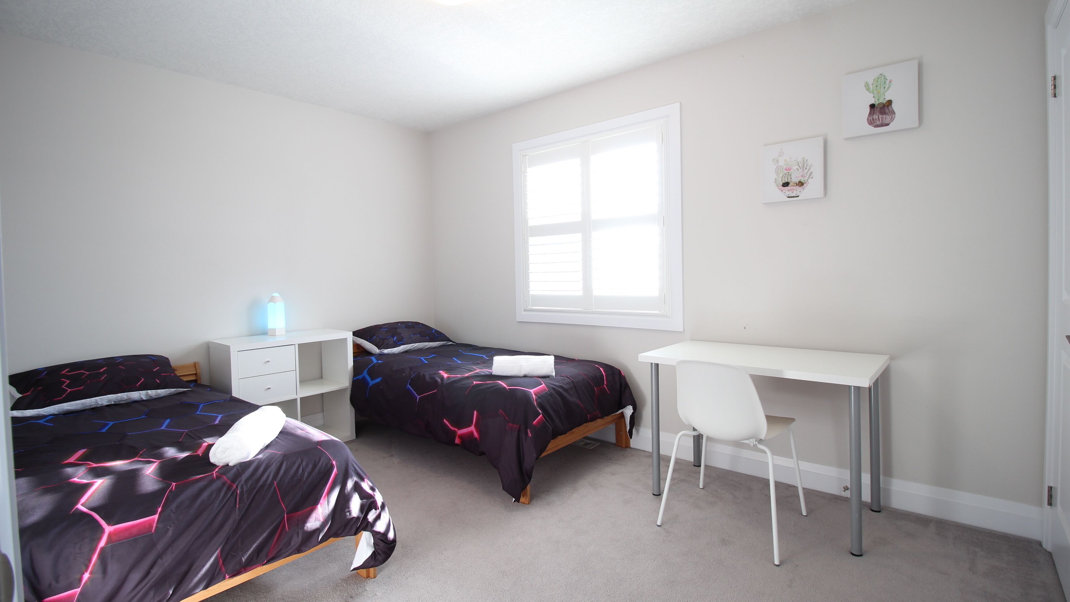 A bedroom with two beds, a desk, and a chair.