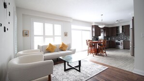 Un salon moderne comprenant un canapé, des fauteuils, une table basse en verre et un coin repas avec une table et des chaises.