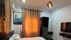 Une chambre d’hôtel avec un lit, des rideaux, un tableau, une télévision et un bureau.