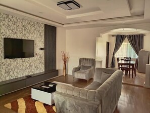 Un salon moderne avec un canapé d’angle gris, un téléviseur à écran plat et un coin repas comprenant une table et des chaises.