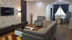 Un salon moderne avec un téléviseur à écran plat, des canapés gris, une table basse et un vase décoratif.