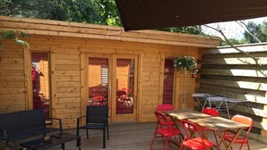 A wooden deck with a table and chairs, a bench, and a covered area with a hanging plant. - Chalet le photinia (Figari)