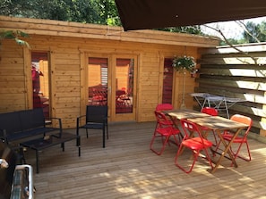 A wooden deck with a table and chairs, a bench, and a covered area with a hanging plant.