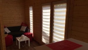 A cozy cabin interior with a wooden interior, a sofa, a small table, and a bed with a red accent. - Chalet le photinia (Figari)