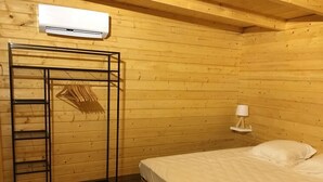 A wooden cabin room with a bunk bed, a metal shelf unit, a wall-mounted air conditioner, and a bedside table with a lamp. - Chalet le photinia (Figari)