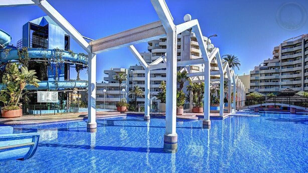 En swimmingpool med krystalklart, blåt vand, omgivet af hvide søjler og plantekasser.