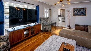 A living room with a large flat-screen TV, wooden entertainment unit, patterned armchair, sofa, and a unique ceiling light fixture. - Luxurious Mid-Century-Retreat (Ogden)