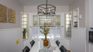 A dining room with a white table, black chairs, a patterned runner, a vase with flowers, and a pendant light. - Luxurious Mid-Century-Retreat (Ogden)