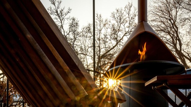 A wooden bench with a metal frame, a fire pit, and a building with a chimney in the background. - Luxurious Mid-Century-Retreat (Ogden)