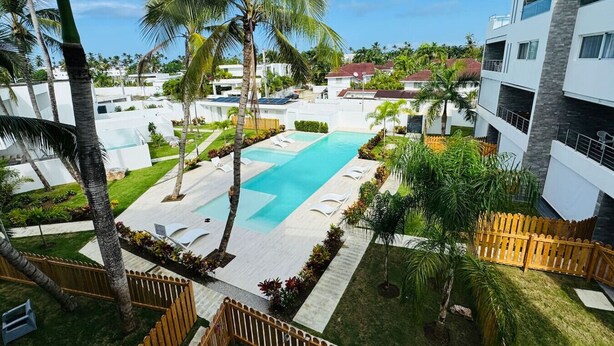 A modern hotel with a swimming pool, palm trees, and a view of the surrounding buildings.