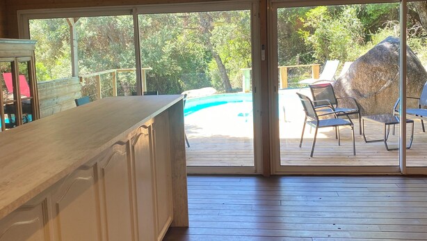 Une cuisine spacieuse dotée d’un plan de travail en bois et de grandes portes-fenêtres coulissantes donnant sur une terrasse extérieure avec une piscine et des chaises.