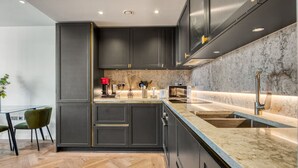A modern kitchen with dark cabinetry, a marble countertop, and a wooden herringbone floor. - Hyde Park Elegenace 2BR 2BA Balcony (London)