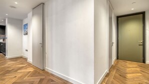 A hallway with wooden flooring and white walls, leading to a room with a green door. - Hyde Park Elegenace 2BR 2BA Balcony (London)