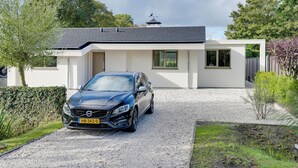 A modern house with a gravel driveway, a parked car, and a garden.
