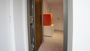 A hallway with a white door, a sliding door, and a white refrigerator with an orange top.