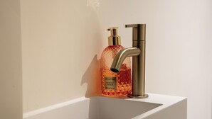 A bathroom with a white sink, a gold faucet, and a bottle of cream soap.