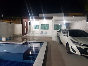 Uma casa moderna com piscina, carro e área de refeições.