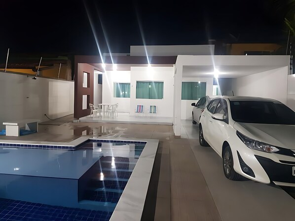 Une maison moderne avec une piscine, une voiture et un coin repas.