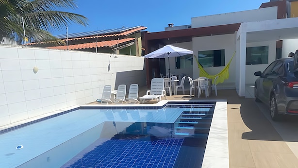A swimming pool with tiled flooring, lounge chairs, and a car parked nearby. - Casa Encanto da Barra (Barra de São Miguel)