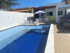 Une piscine dont le fond est recouvert de carrelage, avec des chaises longues et une voiture garée à proximité.