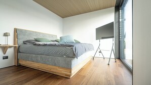 A modern bedroom with a wooden floor, a bed with grey bedding, a wooden headboard, and a large window. - Brenztal Eco Lodge (Giengen an der Brenz)