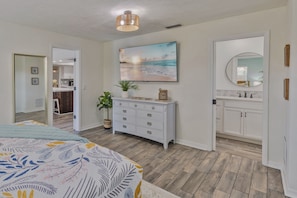 A bedroom with a bed, dresser, and a painting of a beach scene. - Seminole Pool House with Game Room and Fire Pit (Seminole)