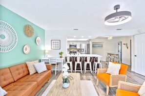 A modern living room with a brown sofa, orange armchairs, and a dining area with white chairs.