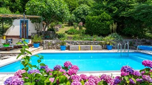 A swimming pool with a stone wall, potted plants, and a small outdoor seating area.