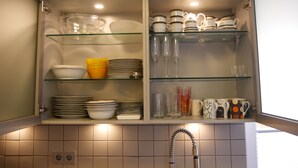 A kitchen with open cabinets displaying dishes, glasses, and a coffee maker. - Vacation cottage Baarsen 30 (Bad Pyrmont)