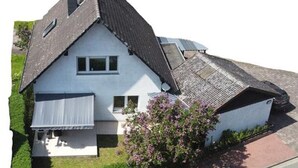 A two-story house with a sloped roof, a small porch, and a garden with flowering plants. - Vacation cottage Baarsen 30 (Bad Pyrmont)