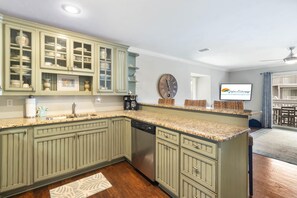 A kitchen with green cabinetry, a built-in dishwasher, and a clock on the wall.