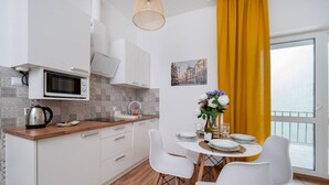 Una cocina moderna con armarios blancos, un microondas y una tetera. Hay una mesa de comedor con sillas y un florero con flores.