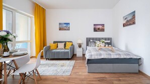 Un dormitorio moderno con cama, sofá, zona de comedor y ventana con cortinas.