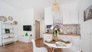 Una cocina moderna con armarios blancos, un comedor con sillas blancas y un televisor montado en la pared.