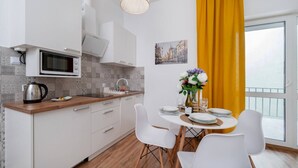 Una cocina moderna con armarios blancos, un microondas y un hervidor. Hay una mesa de comedor con sillas blancas y un jarrón con flores.