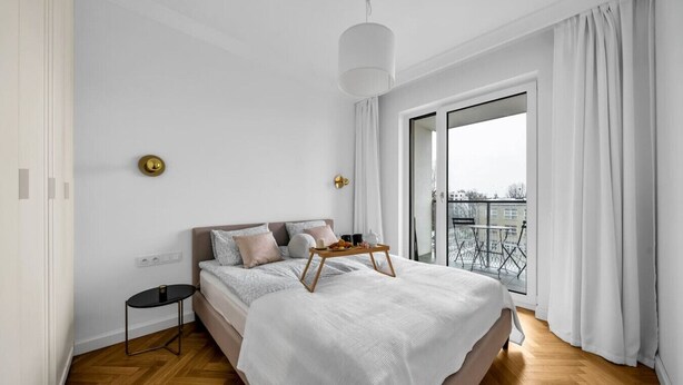 A modern bedroom with a large bed, a bedside table, and a view of a balcony. - Warsaw Żoliborz Apartment- Parking & Two Balconies - by Rentujemy (Warszawa)