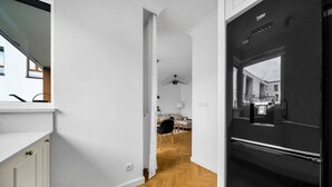A modern kitchen with a black refrigerator, white cabinetry, and a herringbone wood floor. - Warsaw Żoliborz Apartment- Parking & Two Balconies - by Rentujemy (Warszawa)