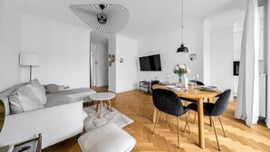 A modern living room with a sofa, a dining table set for two, and a TV mounted on the wall. - Warsaw Żoliborz Apartment- Parking & Two Balconies - by Rentujemy (Warszawa)