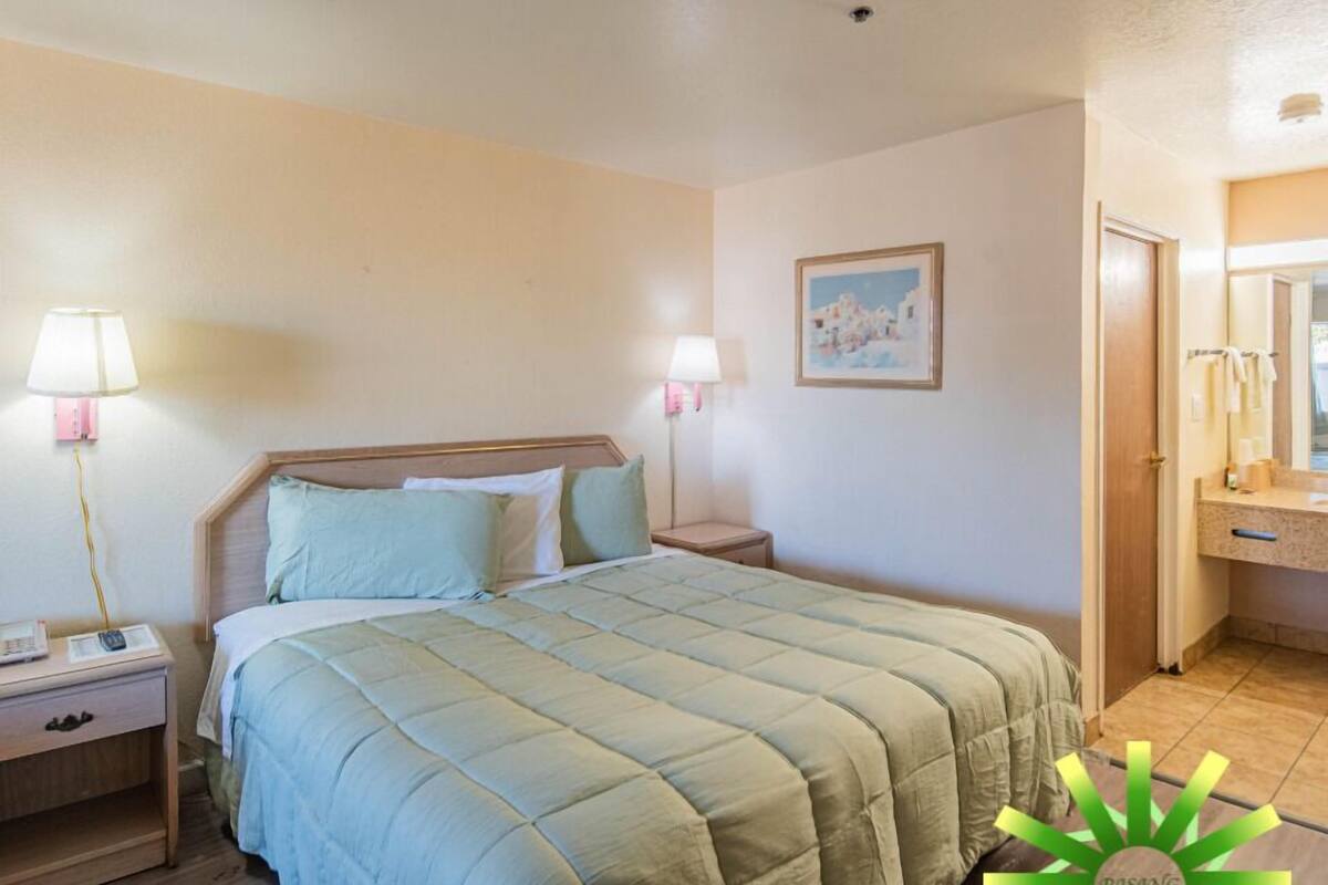 Une chambre à coucher avec un lit, des lampes de chevet, une table de nuit et un tableau encadré au mur. On aperçoit également la salle de bain à travers une porte ouverte.
