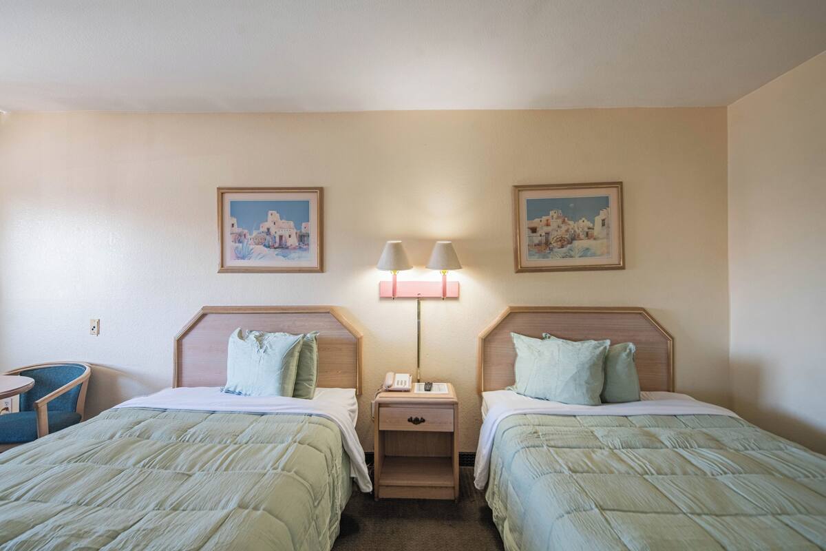Une chambre d’hôtel avec deux lits, un petit bureau, une chaise et une table de chevet avec une lampe.