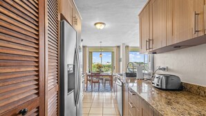 A modern kitchen with wooden cabinets, a stainless steel refrigerator, a granite countertop, and a view of the outdoors. - Ocean View in a central apartment w/ pool and gym (Fajardo)