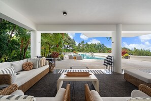 A covered outdoor area with a pool, lounge chairs, and a sofa.