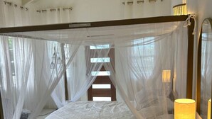 Uma cama com dossel, um abajur e vista para o exterior pelas janelas.