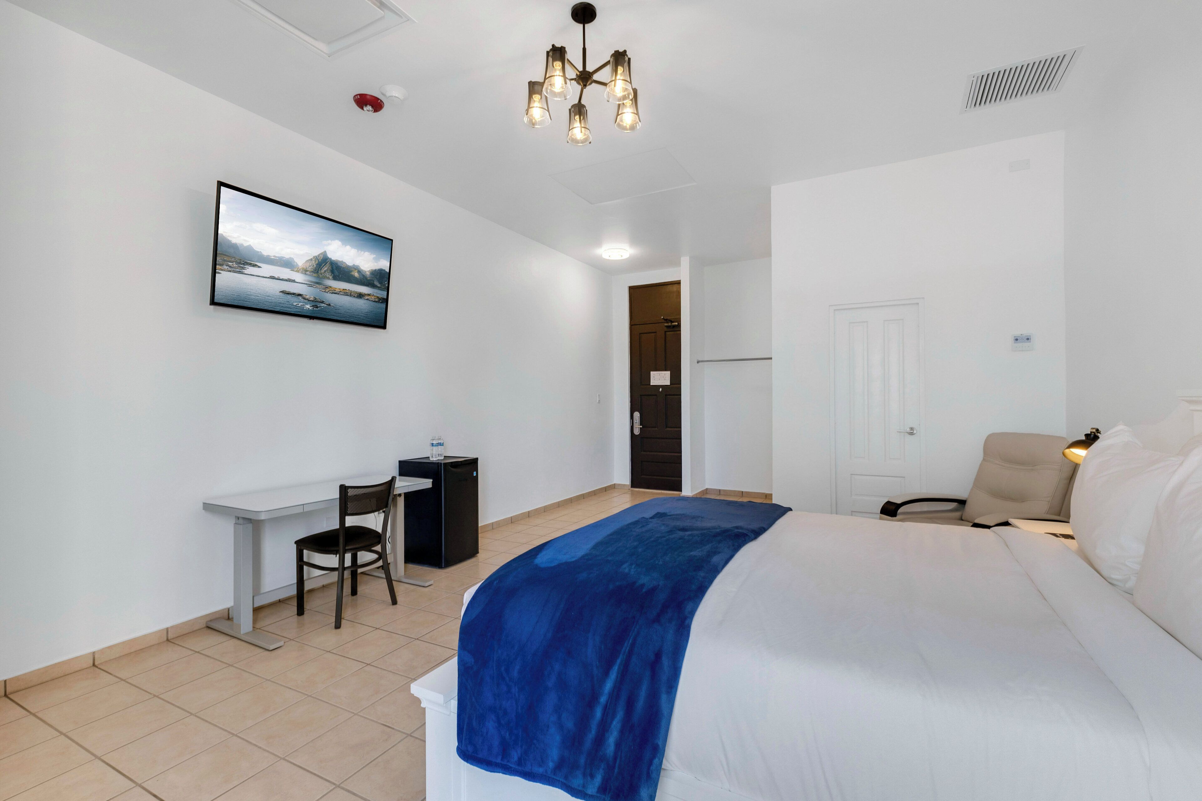 A hotel room with a bed, a desk, a chair, a TV, and a door.