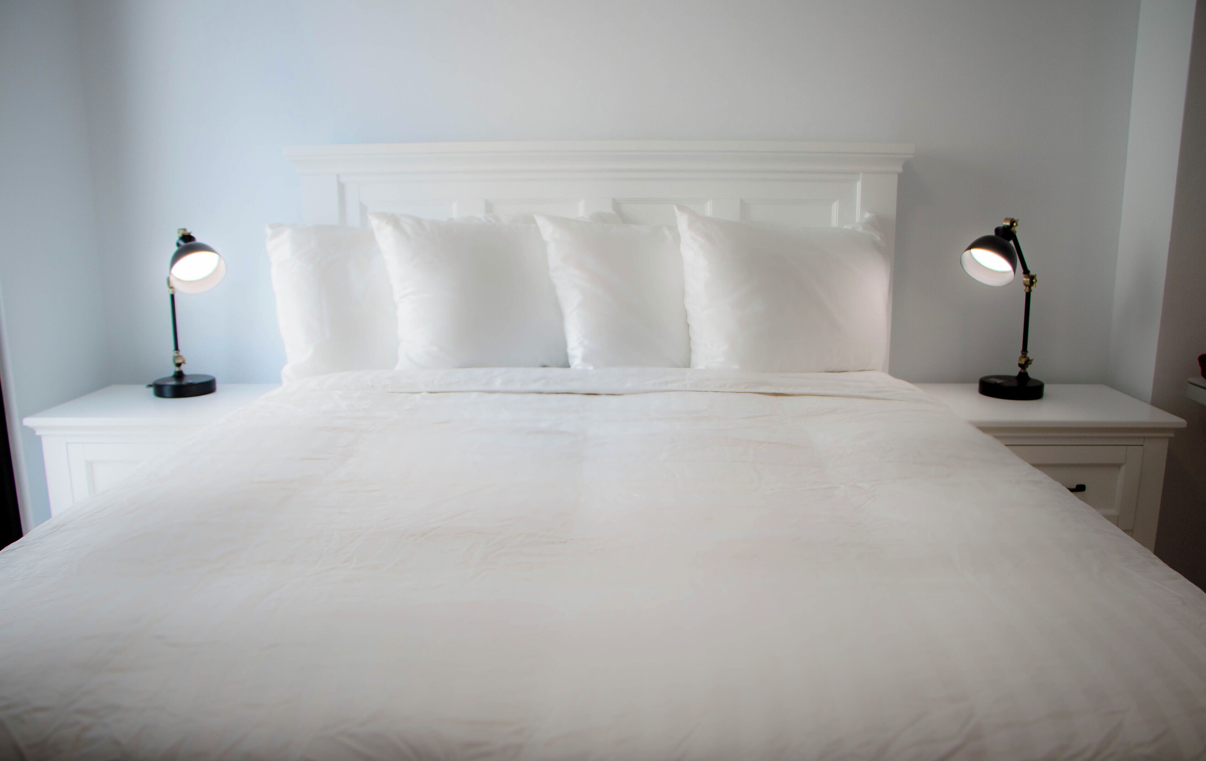 A neatly made bed with white linens and pillows, flanked by two bedside tables with lamps.