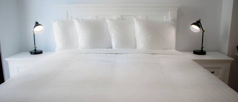 A neatly made bed with white linens and pillows, flanked by two bedside tables with lamps.