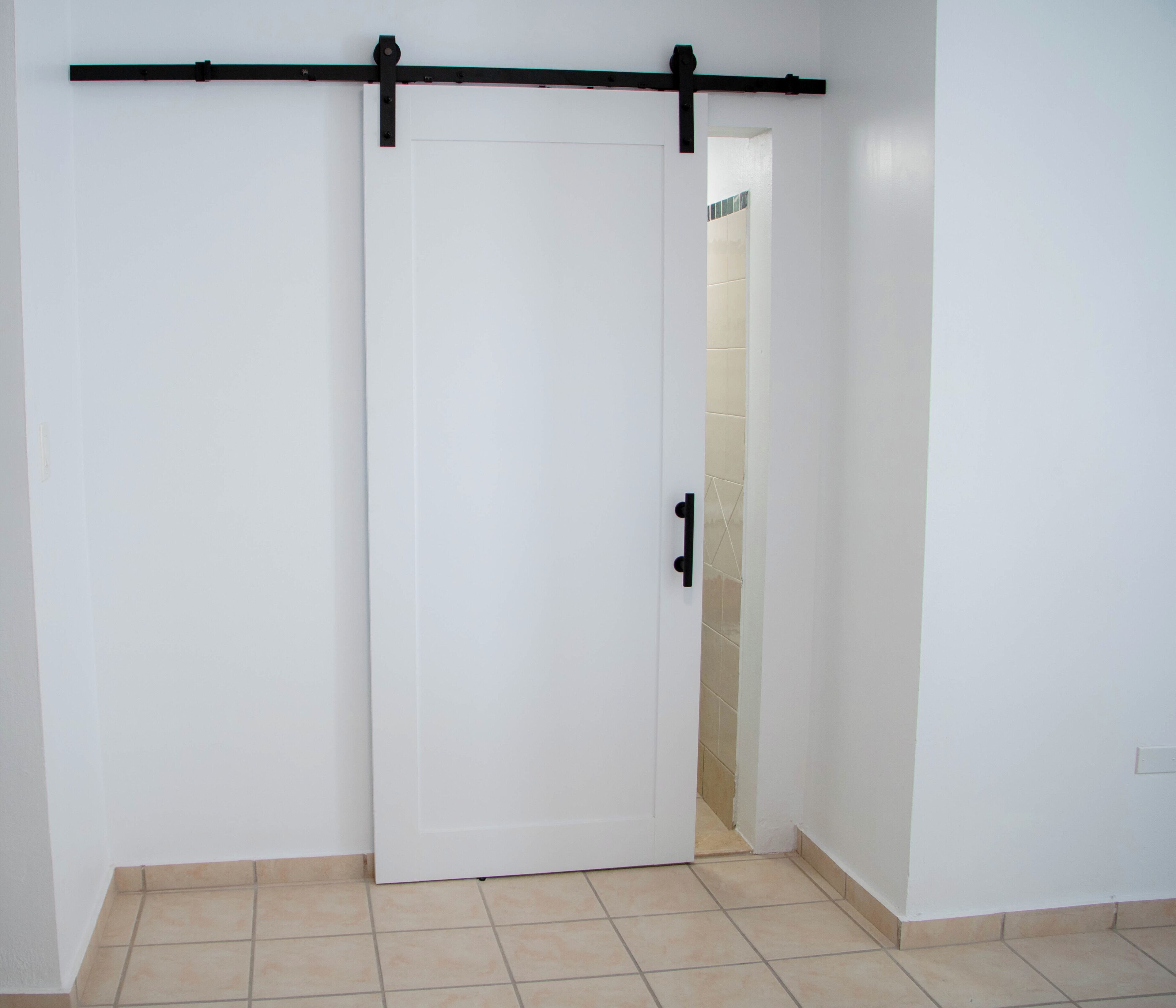 A white door with a black handle, a sliding door mechanism, and a tiled floor.
