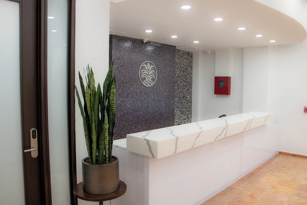 A reception area with a marble counter, a potted plant, a decorative wall, and a fire alarm. - Armas Hotel (San Juan)