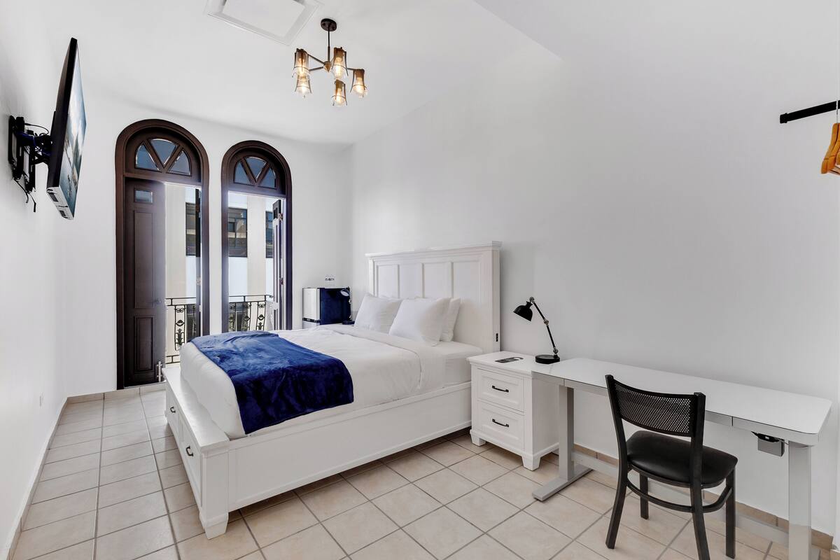 Une chambre à coucher comprenant un lit, une table de chevet, un bureau, une chaise et un téléviseur fixé au mur.